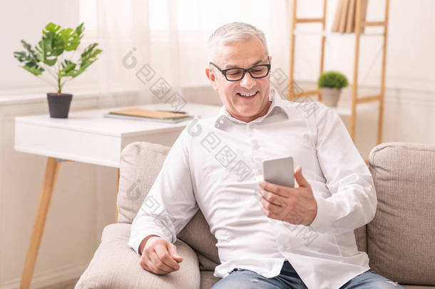 快乐的老人坐在沙发上用智能手机