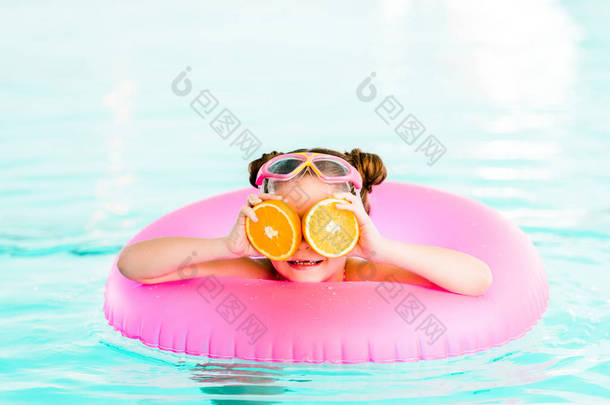 快乐的孩子在游泳池里用充气<strong>环游</strong>泳时, 眼睛附近拿着半橘子