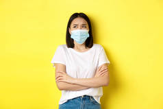 Covid, health care and pandemic concept.身穿白色T恤、戴着医疗面罩的亚洲女人双手交叉胸前，忧心忡忡地抬起头