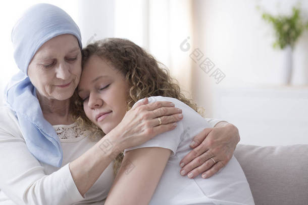 女儿拥抱生病的年迈的母亲与癌症戴着蓝色头巾