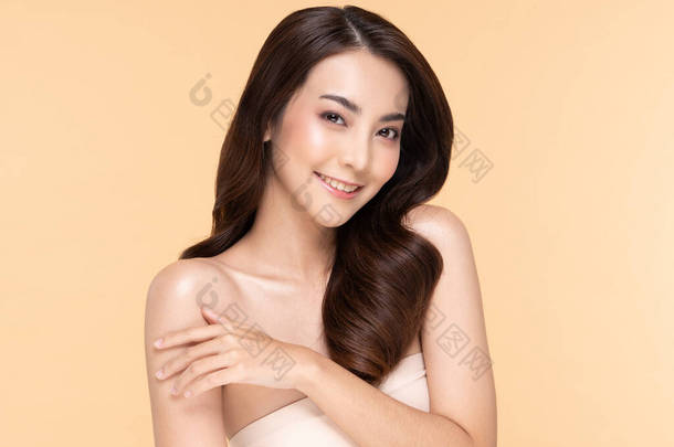 美丽的年轻亚洲女人一边摸着肩膀，一边又开心又快乐，有着<strong>健康</strong>的洁净而新鲜的皮肤，有着米色的<strong>背景</strong>，美容美感