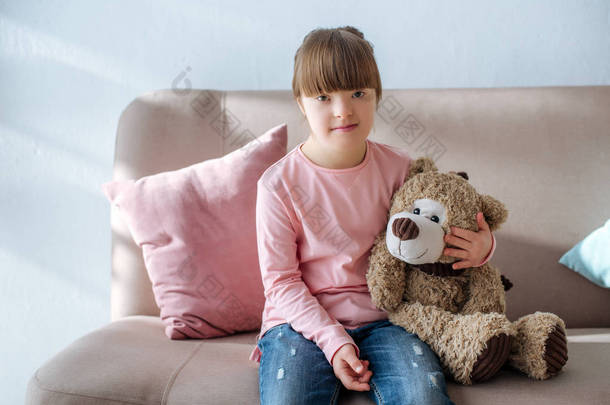 唐氏综合症<strong>儿童</strong>坐在沙发上拥抱泰迪熊