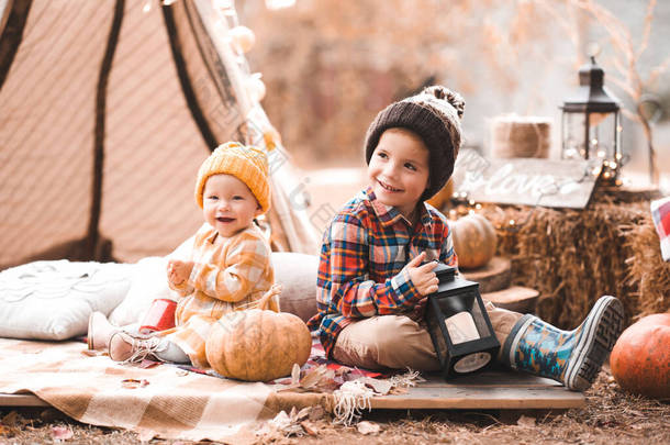 快乐的孩子们穿着秋天的衣服,在户外的灯光下摆着南瓜的姿势.秋天的季节童年. 