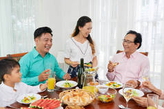 亚洲家庭在餐桌上共度时光，享用沙拉和葡萄酒，闲暇时聊天