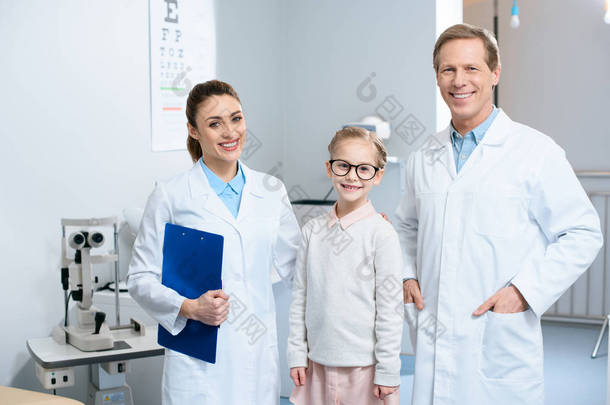 两个微笑的眼科<strong>医生</strong>和小孩子在眼镜站在诊所