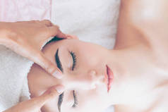 在一个豪华温泉度假胜地，放松了的妇女躺在温泉床上接受按摩治疗师的面部和头部按摩治疗。健康、减轻压力和恢复活力的概念.