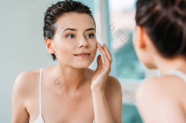 美丽<strong>微笑</strong>的年轻妇女感人的面孔和看镜子在洗手间 