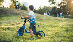 小男孩在公园里骑自行车，看着其他孩子和他们的父母一起散步