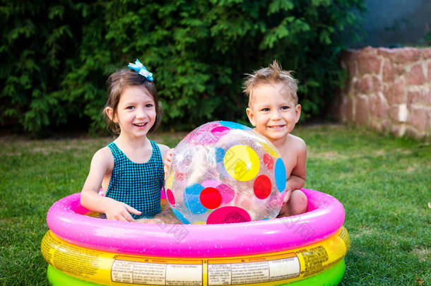 两个孩子带着海滩球在游泳池里。快乐的孩子在充气游泳池后院里玩耍。阳光灿烂的日子,孩子们在游泳池游泳.五彩缤纷的游泳池球健康婴儿<strong>暑期</strong>活动.