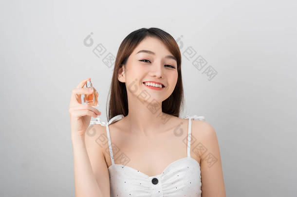 一位美丽的亚洲女子对着相机笑着，手里拿着一瓶带有<strong>迷人</strong>香水的液体