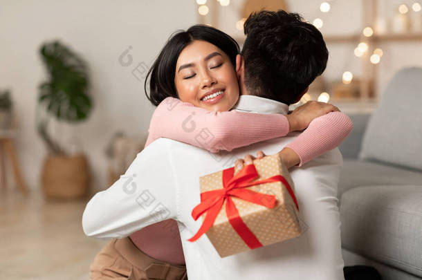欣喜若狂的亚洲妻子拥抱丈夫在家接受圣诞礼物
