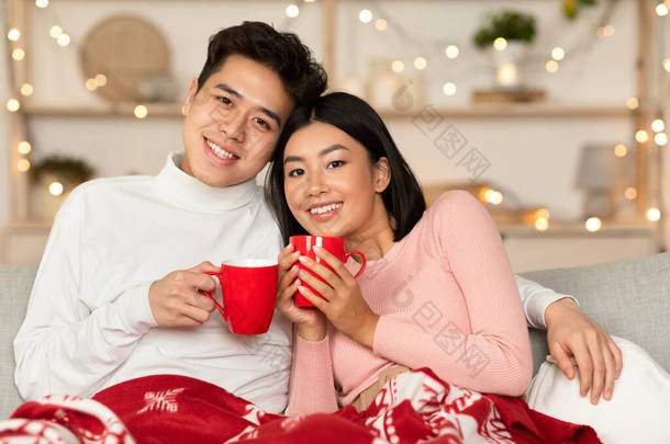 热爱工作的亚洲夫妇抱着咖啡杯坐在家里