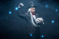 穿着西服、头戴帽子的情绪魔术师，带着魔杖和白兔表演魔术，黑漆漆的房间里挂满了烟雾和闪光的插图