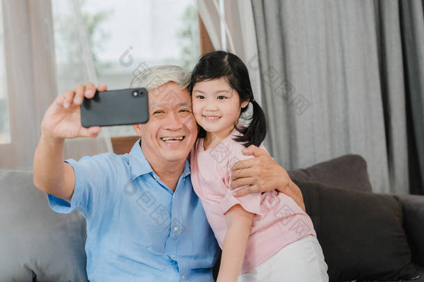 亚洲祖父和孙女的视频电话在家里。4.中国的爷爷很高兴看到这个小女孩用手机打来电话，和她的爸爸妈妈躺在客厅里聊天.