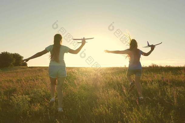 快乐童年的概念。 <strong>梦想</strong>的飞行。 两个女孩在日落时玩玩具飞机. <strong>孩子</strong>们在阳光下,手里拿着一架飞机. 儿童在飞机上玩耍的轮廓