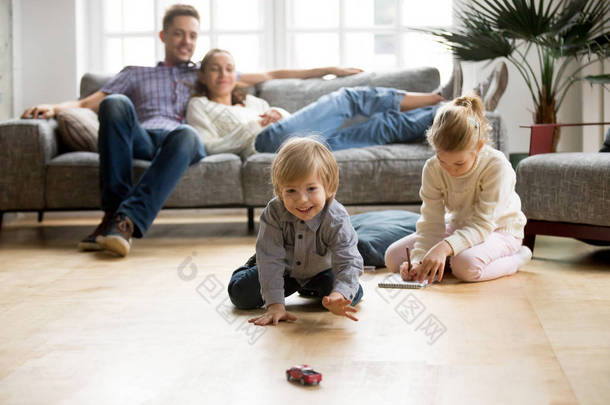 孩子们在地板上玩耍, 父母在家里放松沙发