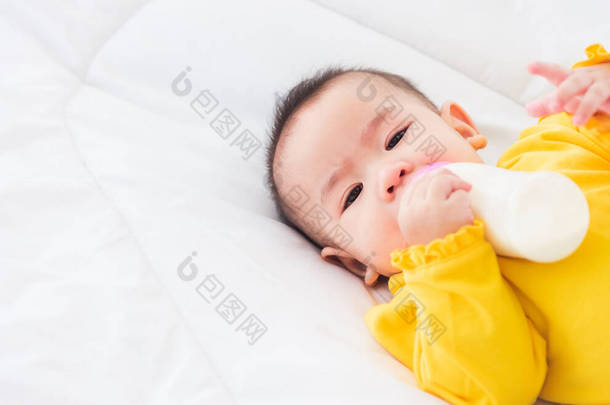 亚洲漂亮的小女孩穿着一件黄色的衣服，吃着睡在白色床上的牛奶，抱着一瓶牛奶的<strong>婴儿</strong>，<strong>婴儿</strong>食品的概念