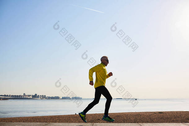 运动服装中老年人的剖面图保持健康的生活方式在海边慢跑, 享受清新的空气, 背景万里无云的蓝天