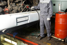 一位汽车修理工从发动机中抽出用过的油.公共汽车上的工人