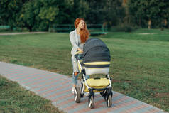 一个年轻的母亲享受公园散步与她的小孩子放松在他的婴儿推车.