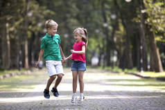 两个可爱的年轻有趣的微笑的孩子, 女孩和男孩, 兄妹, 跳跃和乐趣模糊明亮的阳光明媚的公园小巷绿树 bokeh 的背景。快乐粗心大意的童年概念.