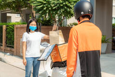 亚洲妇女从盒子里拿起分娩食品袋，供与外界接触或免费与骑自行车的人在前面的房子里接触，以便与外界保持距离，防止感染.