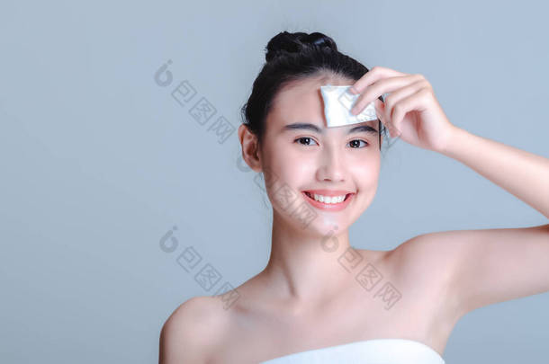 一个迷人的亚洲女人的微笑。用棉质羊毛和爽肤粉来清洁肌肤，使其保持清新、光泽和清洁。在白色的背景下，美容美发的概念被分离出来.