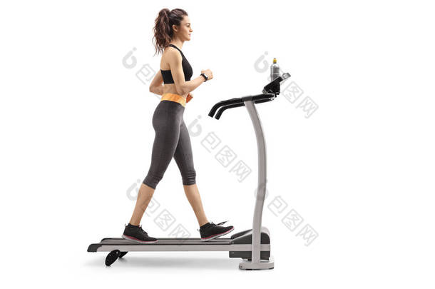 在白色背景下的跑步机上行走的健身妇女的全长剖面照片