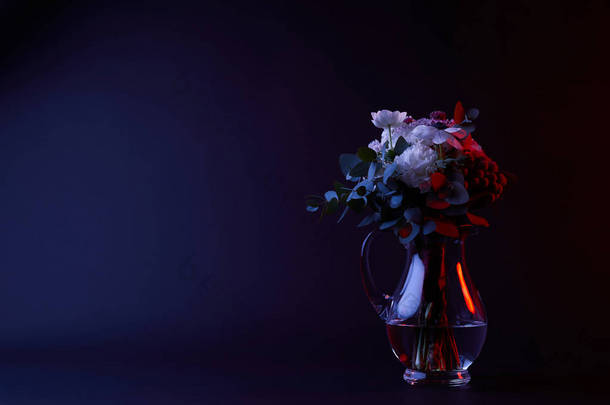 水瓶中不同花朵的花束与水在黑暗中