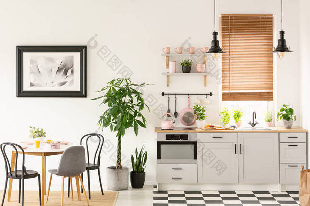 真实照片的明亮的厨房内部与棋盘地板, 粉彩粉红色配件, 新鲜植物和餐桌上的地毯
