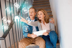 妻子指着手, 而坐在楼梯上的丈夫, 并使用数字平板电脑, 智能家居的概念