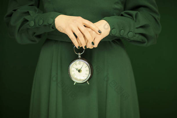 美丽的女人身材绿色的衣服与绿色背景举行复古钟, 色调绿色