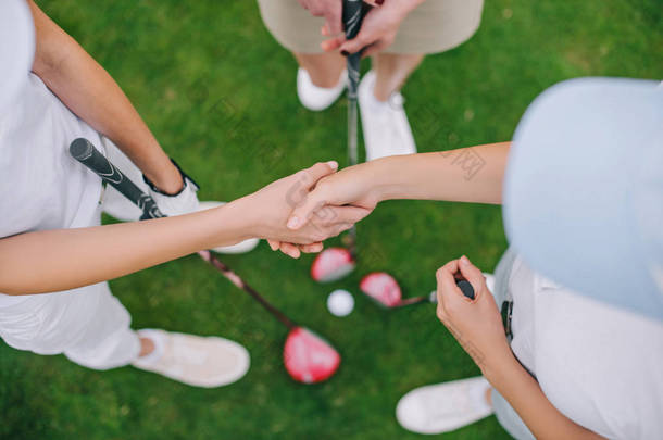 高尔夫俱乐部女高尔夫球运动员站立在绿色草坪上握手的头顶视图