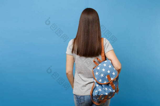 背部后视图的年轻黑发女学生在休闲服装与背包站在蓝色背景孤立。高中大学的教育。复制广告空间