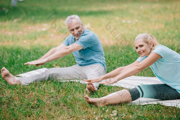微笑的男人和女人练习伸展瑜伽姿势，而坐在瑜伽垫