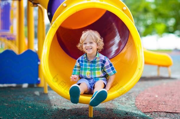 孩子们在户外操场上玩耍。孩子们在学校或幼儿园院子里玩耍。活泼的孩子在彩色的滑动和摆动。儿童健康的夏季活动。小男孩在户外攀爬.