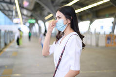 一名年轻女子站在地铁站站台上，戴着口罩，保护Covid-19，这是新的正常旅行理念.