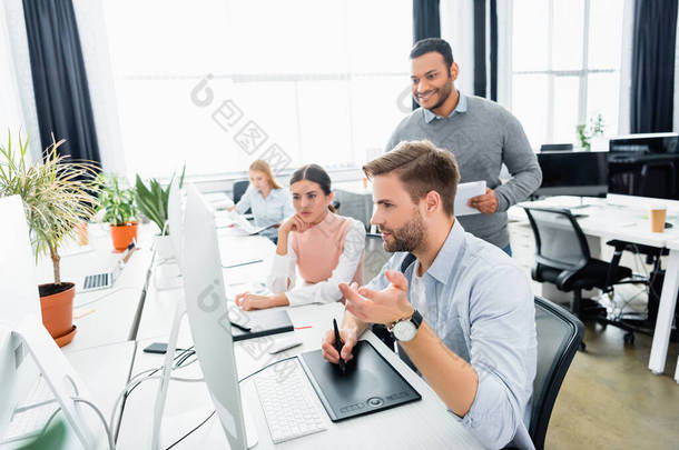 在<strong>办公室</strong>多<strong>文化</strong>同事身边使用图形平板电脑的商人 