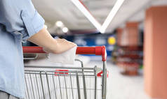 妇女手握购物车的手柄与纸巾在超市,特写镜头.肠病毒爆发期间在公众地方采取的预防措施