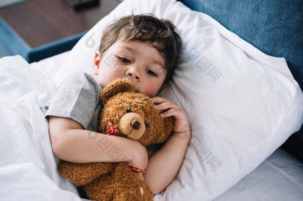 可爱的孩子躺在床上与泰迪熊在家里 