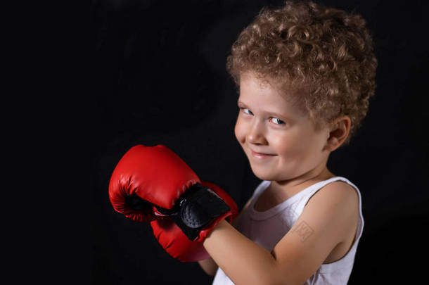 穿着红色拳击手套的小男孩，背景是黑色的。 运动、儿童拳击.