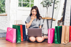 美丽的女人购物在线与笔记本电脑的技术和五颜六色的购物袋坐在地板上在家