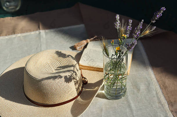 玻璃杯中的野花，一本打开的书，一个女人的夏帽，上面铺着丝带，桌上铺着亚麻布桌布，<strong>还有</strong>夏日黄昏的阳光的阴影，村舍的核心美学概念