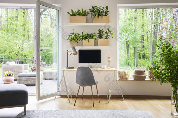 鼓舞人心的工作空间内部的自由职业者与计算机上的木制办公桌, 白色的墙壁和自然的看法在后院外