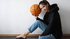 年轻美丽的女孩篮球运动员摆在地板上和举行球