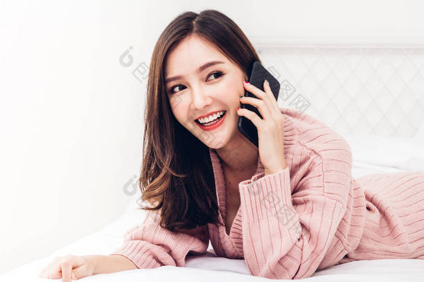 快乐的女人在家用智能手机放松地在床上聊天。科技与交流的概念