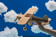 图片说明妇女在白色蓬松的云彩附近手持木制玩具飞机，这些云彩是用蓝色孤立的棉质羊毛制成的