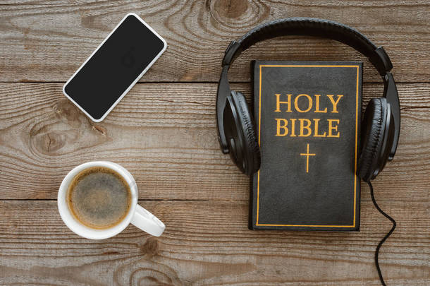 在木制桌面上的耳机, 智能手机和咖啡的圣圣经的顶部视图