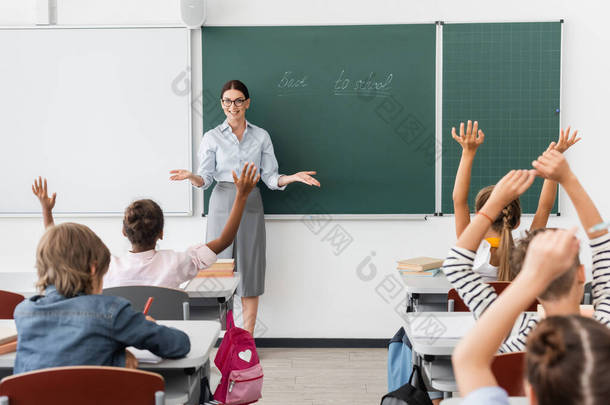 多种族学生手牵手站在空中，教师张开双臂站在黑板旁边，背对着学校字母