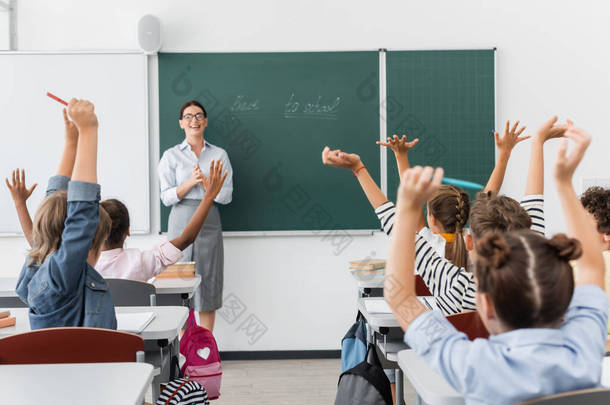 后见多文化学生手牵手在空中，老师站在黑板旁边，背对着学校的字母
